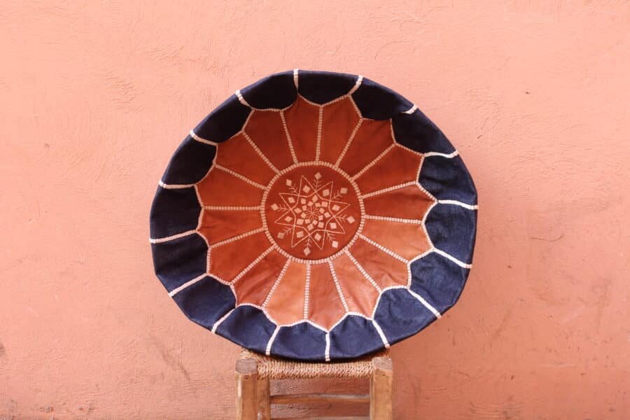 Handcrafted leather pouf ottoman with intricate stitched patterns, featuring a combination of tan and navy leather, perfect for stylish home decor