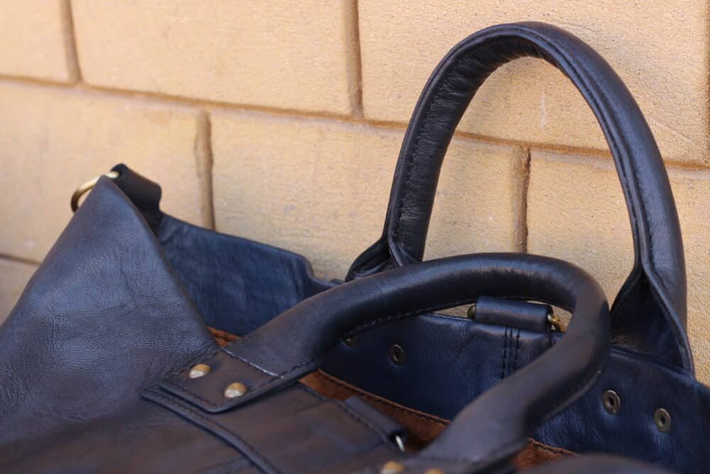 Leather Messenger Bag with essentials like documents and gadgets displayed on a desk.