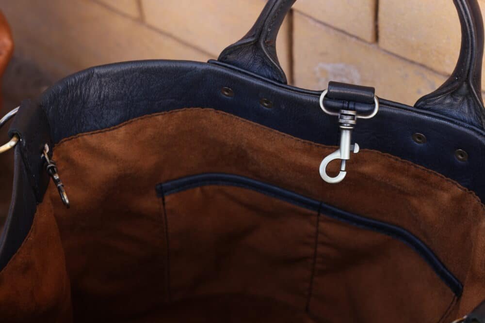 Leather Messenger Bag hanging on a coat rack next to a jacket.