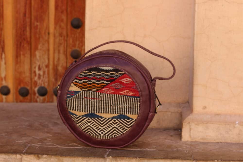 Round leather crossbody bag in beige with adjustable strap and modern design.