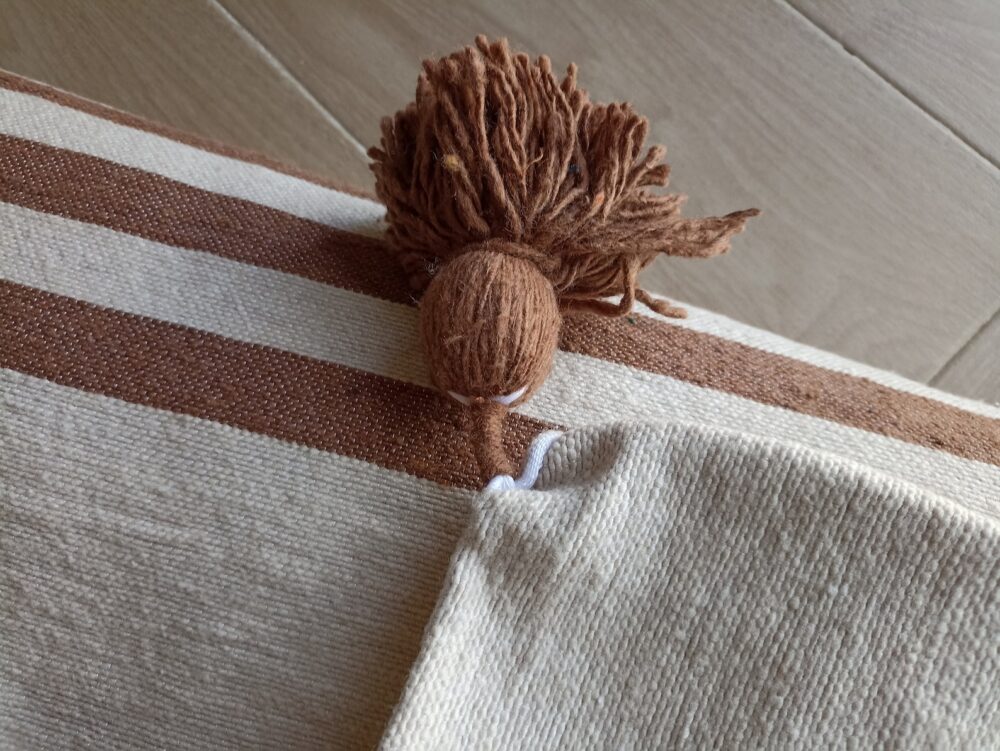 Handcrafted Moroccan striped blanket with pom-poms in earthy tones