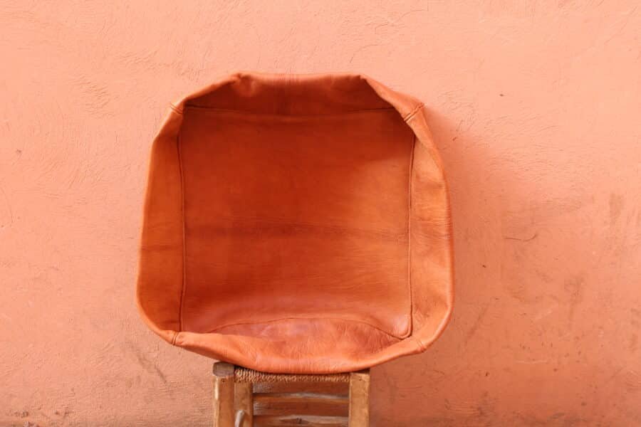 Handmade Caramel Moroccan Leather Pouf on a rustic chair with peach-colored background